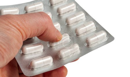 Close-up of a man's hand tightly clutching a pack of pills. the main object is isolated on a white background.
