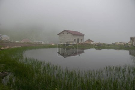 View of a rustic house reflected in a lake on a foggy Plateau