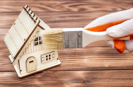 Téléchargez les photos : Concept de réparation de maison. Main dans le modèle de peinture à gants de la maison sur fond en bois. - en image libre de droit