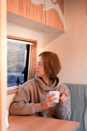 Photo for Moment of tranquility as a young man enjoys a warm beverage inside the cozy wooden interior of his self-converted van, showcasing a DIY travel lifestyle. - Royalty Free Image