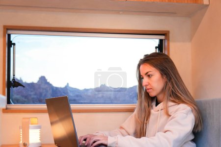 A digital nomad working remotely in a van sits in front of a laptop computer.