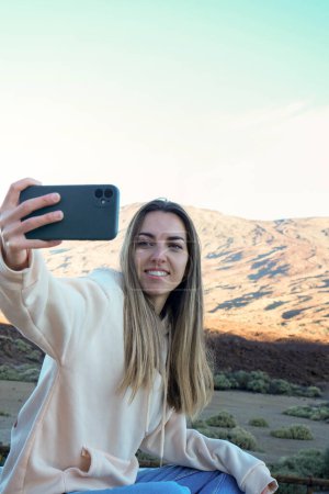 A woman captures a moment by taking a selfie with her smartphone in front of the majestic Teide mountain.