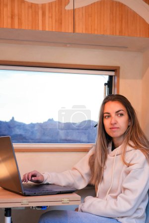 A digital nomad sitting at a desk inside a van, using a laptop computer to work remotely.
