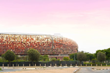 The iconic Soccer City Stadium in Johannesburg basks in the warm glow of a sunset, showcasing its distinctive mosaic facade against the evening sky.