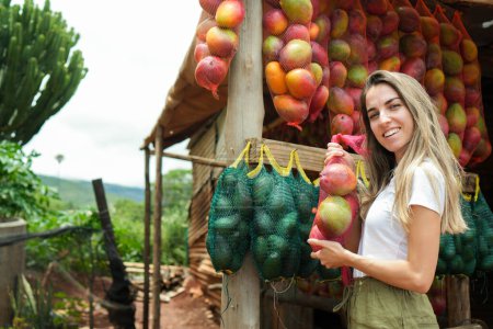 Eine glückliche Frau kauft an einem bunten Obststand entlang einer Landstraße in Afrika reife Mangos und verkörpert damit die Lebendigkeit der lokalen Märkte..