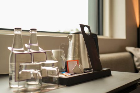 Téléchargez les photos : Une table dans une chambre d'hôtel avec un plateau de verres à eau et une bouteille d'eau pour les clients. - en image libre de droit