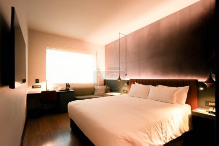 Ein luxuriöses Bett mit einer stilvollen Lampe und einem eleganten Tisch in einem großzügigen Hotelzimmer, das ein anspruchsvolles und komfortables Ambiente schafft.