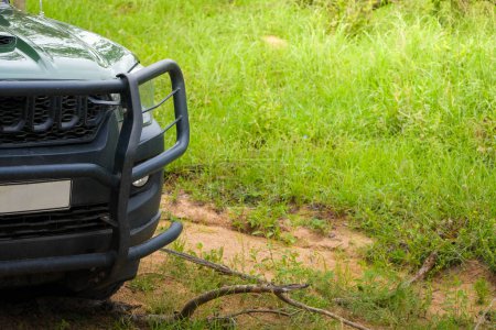 Un vehículo todoterreno 4x4 se está embarcando en un viaje a través de la exuberante hierba y el terreno accidentado del Parque Nacional Kruger. El foco está en el panel frontal y el parachoques robusto del vehículo, destacando su preparación para el desafiante sendero natural