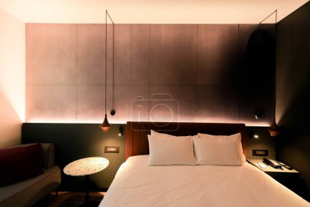 Ein weißes Bett steht neben einem Nachttisch in einem luxuriösen Hotelzimmer und schafft eine gemütliche und elegante Atmosphäre.