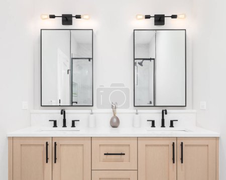 Foto de Un baño moderno con un gabinete de tocador de madera, grifos negros, encimera de mármol blanco y espejos cuadrados con borde negro. - Imagen libre de derechos