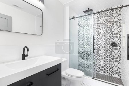 Téléchargez les photos : Une salle de bain avec un meuble lavabo gris, lavabo blanc, et une douche carrelage noir et blanc. - en image libre de droit