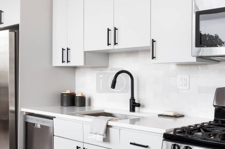 Foto de Un hermoso tiro de detalle de cocina blanca con una pared posterior de azulejos, gabinetes blancos, electrodomésticos de acero inoxidable, y hardware negro y grifo. - Imagen libre de derechos
