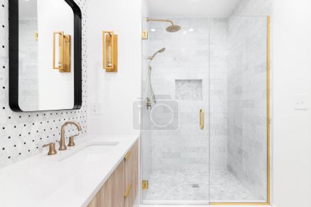 Téléchargez les photos : Une salle de bain avec une armoire en bois, dosseret carrelé, robinets et lumières dorées, et une douche carrelée en marbre. - en image libre de droit
