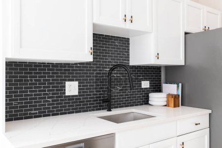 Photo for Kitchen sink detail shot with white cabinets, small black marble subway tile backsplash, and a black faucet. - Royalty Free Image