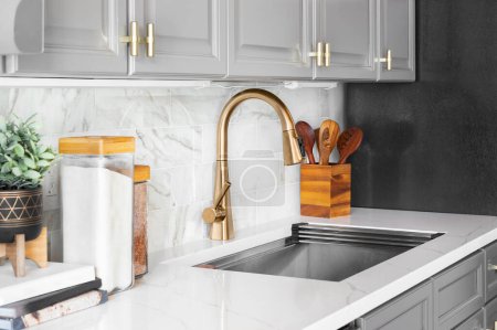 Foto de A kitchen sink detail shot with grey cabinets, a marble subway tile backsplash, and gold hardware and faucet. - Imagen libre de derechos