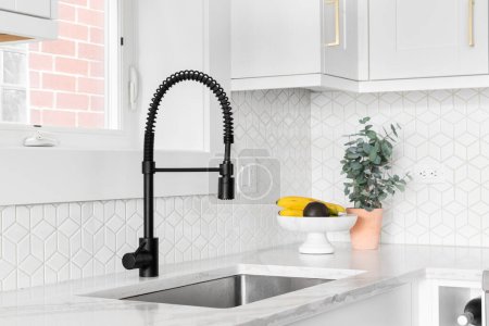 Photo for A farmhouse kitchen sink detail shot with a black faucet, mosaic tile backsplash, marble countertops, and white cabinets. - Royalty Free Image
