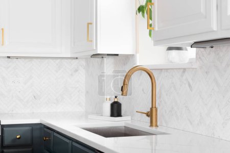 Photo for Sink detail shot in a luxury kitchen with herringbone backsplash tiles. white marble countertop, and gold faucet. - Royalty Free Image