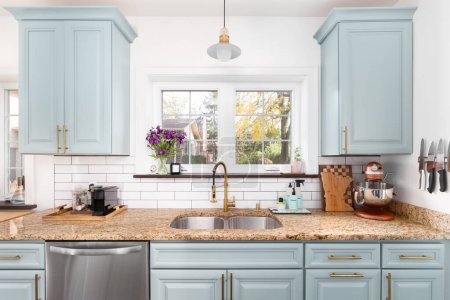Téléchargez les photos : A light blue kitchen detail with a granite countertop, gold faucet and light, and a white subway tile backsplash. - en image libre de droit