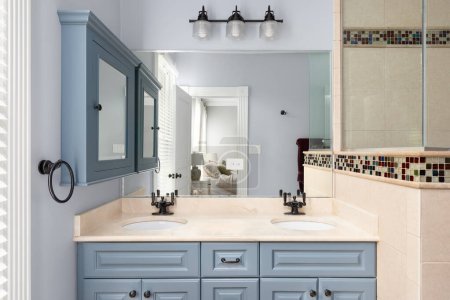 Photo for A bathroom with blue cabinet and medicine cabinet, a marble countertop, tiled shower, and view towards the primary bedroom. - Royalty Free Image