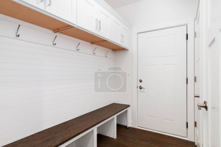 A mudroom with a dark wood floor and bench, white built-in cabinets and organization, and shiplap mounted on the wall.