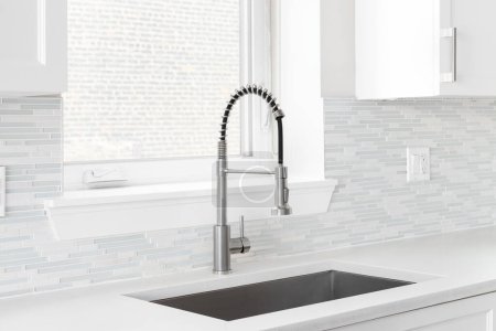 Photo for A kitchen faucet detail with a polished stainless steel faucet, a glass and stone mosaic tile backsplash, and white cabinets. - Royalty Free Image