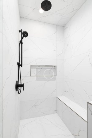 Téléchargez les photos : Une douche de luxe avec des murs en marbre blanc et le sol, un robinet noir et pomme de douche, et une étagère de niche en marbre. - en image libre de droit
