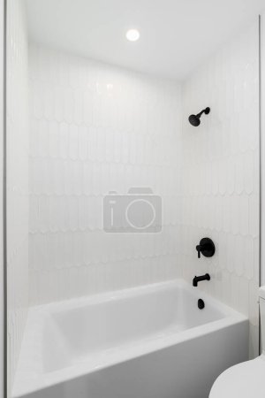 Téléchargez les photos : Une douche et une baignoire avec carrelage piquet blanc et robinet noir et pomme de douche. - en image libre de droit