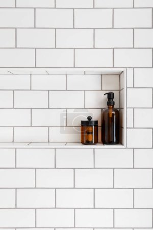 Téléchargez les photos : Une étagère de douche avec des carreaux de métro blanc et des bouteilles de savon brun assis dans la niche. - en image libre de droit