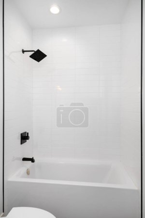 Téléchargez les photos : Une douche et une baignoire avec carrelage de métro blanc et pomme de douche et robinet noirs. - en image libre de droit