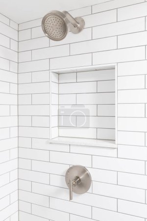Téléchargez les photos : Un détail de douche salle de bains avec des murs de tuiles de métro blanc, une étagère de niche intégrée et une pomme de douche en bronze. - en image libre de droit