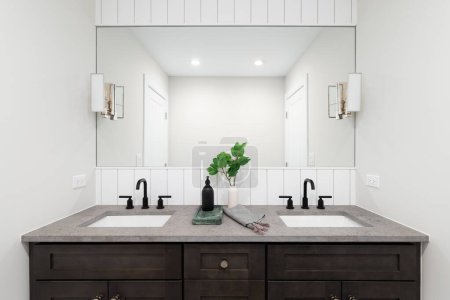 Photo for A bathroom with a dark wood vanity cabinet, quartz countertop, shiplap wall, and bronze lights mounted on the mirror. - Royalty Free Image