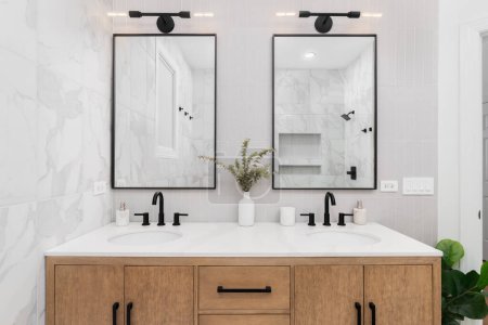Photo for A bathroom with marble and stacked vertical subway tiles, a white oak vanity cabinet, black framed square mirrors and faucets, and marble countertop. - Royalty Free Image