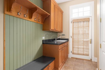 Photo for An entryway mudroom with wood cabinets and shelving, green wood paneling, and a grey bench and countertop with a sink. - Royalty Free Image