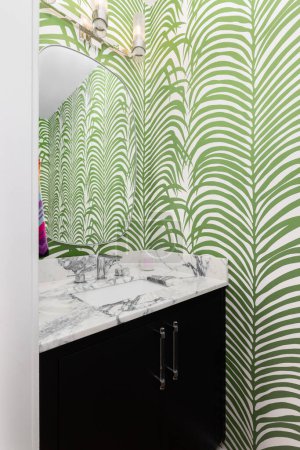 Foto de Un baño con fondo de pantalla verde y blanco, un armario negro, encimera de mármol y luz montada encima del espejo. - Imagen libre de derechos