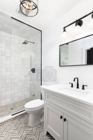 Photo for A bathroom with a white cabinet and countertop, black and gold light fixtures, and a stripe tile floor, and show with square and stripe tiles. - Royalty Free Image