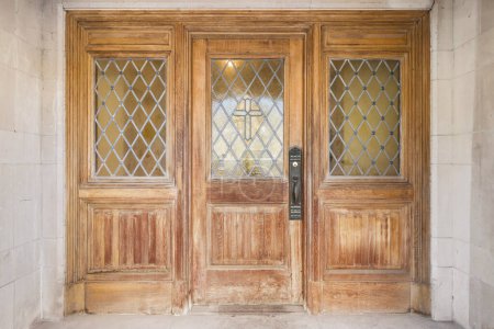 The wooden front door of a reformed church turned into a home with a cross built into the pattern of the glass.