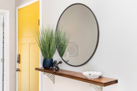 A cozy entryway a bright yellow front door, decorations on a shelf, and a large circular mirror hung on the wall.