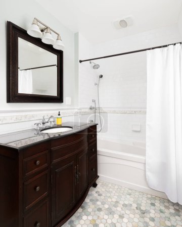 Téléchargez les photos : Une salle de bain avec un meuble lavabo en acajou foncé, carrelage hexagonal, et une douche avec des carreaux de métro blanc. - en image libre de droit