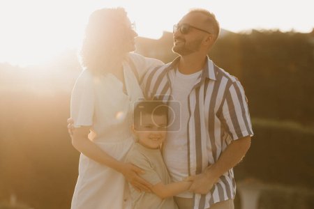 Téléchargez les photos : Father, mother and son are hugging in an old European town. Happy family in the evening. Dad is smiling at his family at sunset. - en image libre de droit