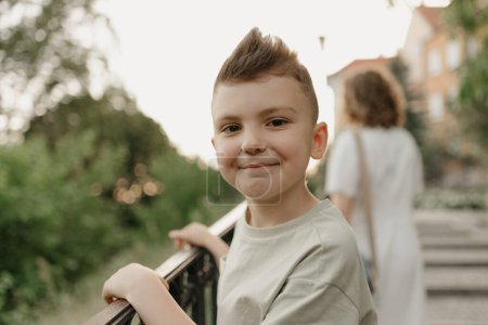 Photo for The close portrait of a boy near the parapet on the green cobbled street of an old European town. Happy fellow in the evening. Tourists at sunset. - Royalty Free Image