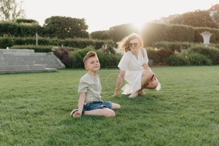 Téléchargez les photos : Mother and son are having fun in the garden of an old European town. Happy family in the evening. A boy is showing somersaults to his parent at sunset. - en image libre de droit