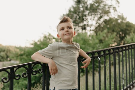 Photo for The close portrait of a boy near the iron stair railing on the green street of an old European town. Happy fellow in the evening. Young tourist at sunset. - Royalty Free Image