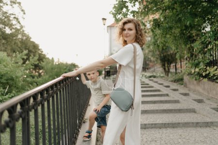 Téléchargez les photos : Mother and son are staring near the parapet on the green cobbled street of an old European town. Happy family in the evening. Tourists at sunset. - en image libre de droit