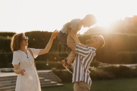 Téléchargez les photos : Father, mother, and son are having fun in an old European town. Happy family in the evening. Dad is throwing his little boy up near mom at sunset. - en image libre de droit