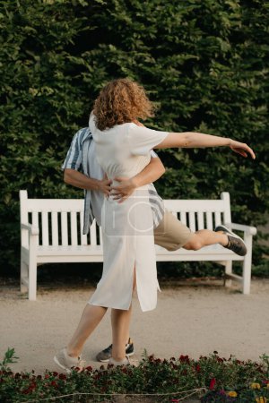 Téléchargez les photos : Un homme danse avec une femme aux cheveux bouclés dans le jardin le soir. Un couple heureux avec des feuilles vertes en arrière-plan. - en image libre de droit