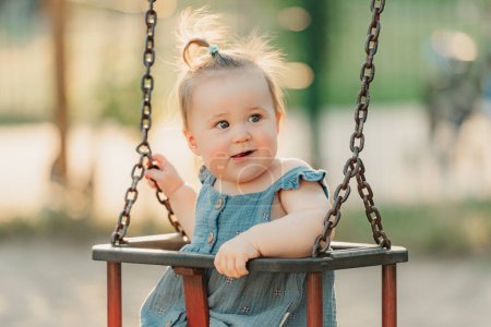 Photo for Toddler baby girl on a swing on the warm summer evening. Mother is swinging her young daughter on a sunny playground. - Royalty Free Image