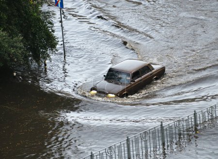Photo for Kyiv, Ukraine - July 7, 2023: A brown car passes through a flooded road area after heavy rain - Royalty Free Image