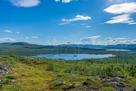 Schöner Sommerblick aus dem weiten schwedischen Hochland, mit vielen kleinen Seen, umgeben von grüner Vegetation, hellem Sonnenlicht und einer Bergkette in der Ferne