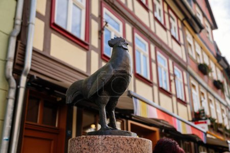 Téléchargez les photos : Wernigerode, Saxony-Anhalt, Germany, 29 October 2022:  Statue of a hen or rooster, Historic old vintage colored timber frame houses in medieval town, UNESCO World Heritage city - en image libre de droit