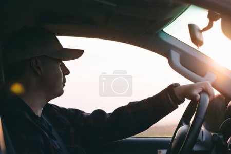 Ein Mann ist zu sehen, wie er ein Auto fährt, in dem die Sonne durch die Windschutzscheibe scheint.